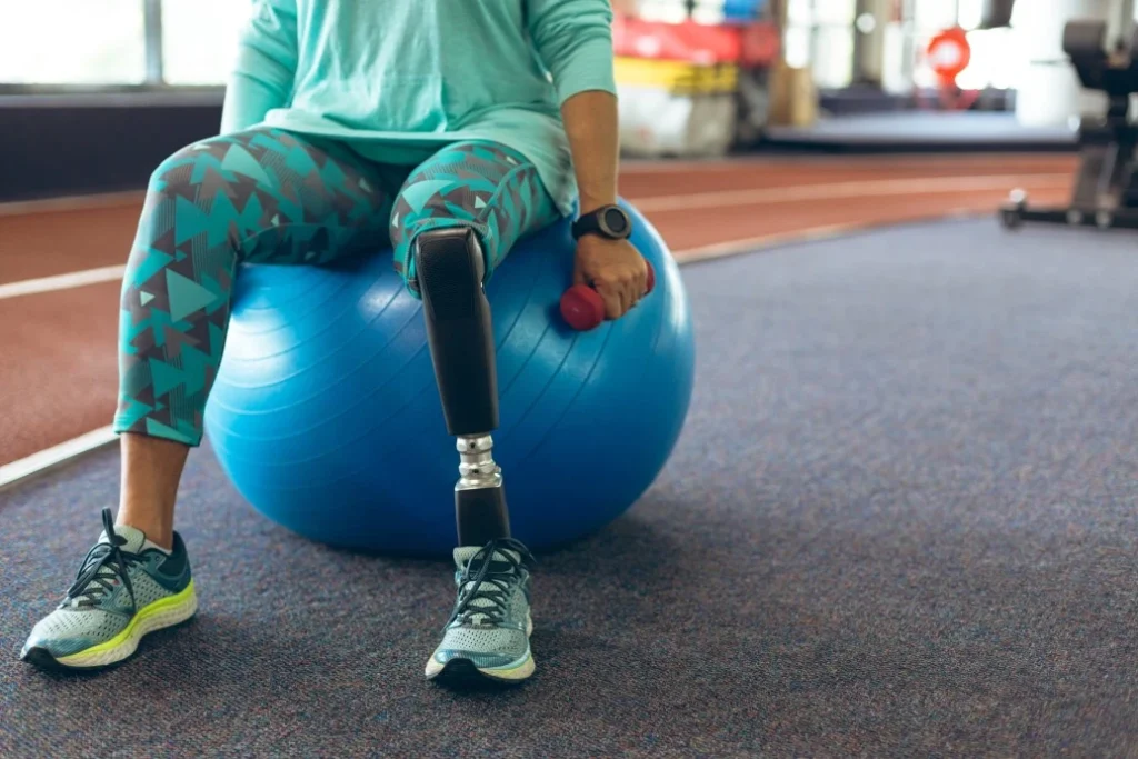 Disabled person with amputated leg sitting on exercise ball and holding weight in one hand